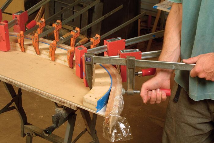 Start clamping at the middle and work toward the ends, using a clamping caul made from five or six strips of 3⁄16-in.-thick birch plywood to prevent bumps.
