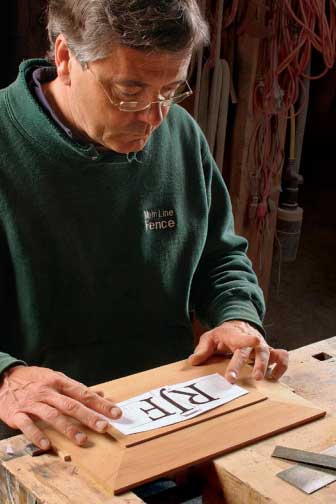 A woodworker lining up a template of letters to carve on a piece of wood.