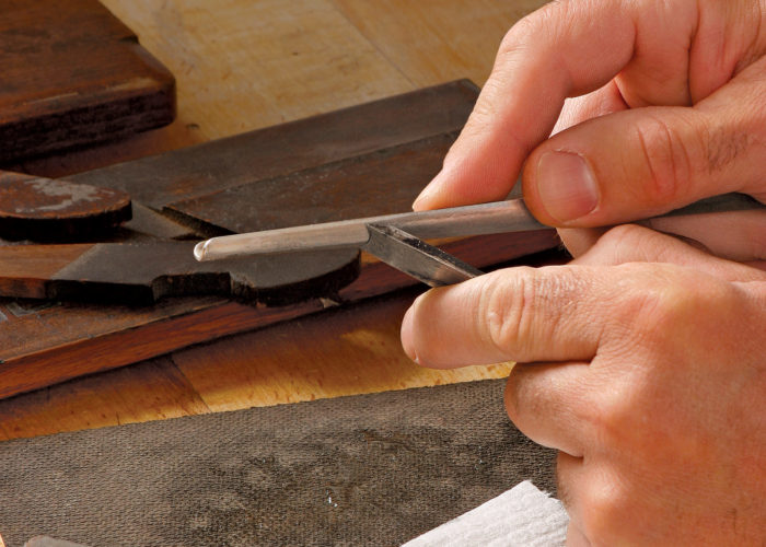 Hold the blade firmly, bracing your hand against a benchtop, and carefully hone the bevel with a slipstone.