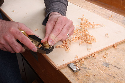Matt Kenney uses a block plane to flush up solid edge banding on a plywood panel.