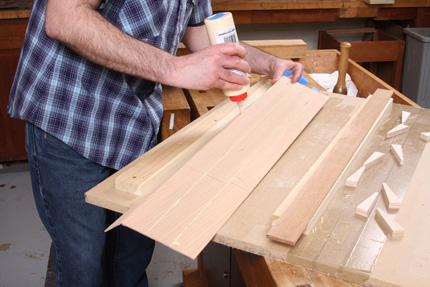 Matt holds the veneer, that is taped on the backside. He applies a bead of glue to the edge of the veneer.