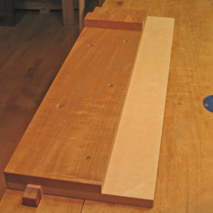 shooting board shown on a workbench with a low-friction plastic strip on the right side.