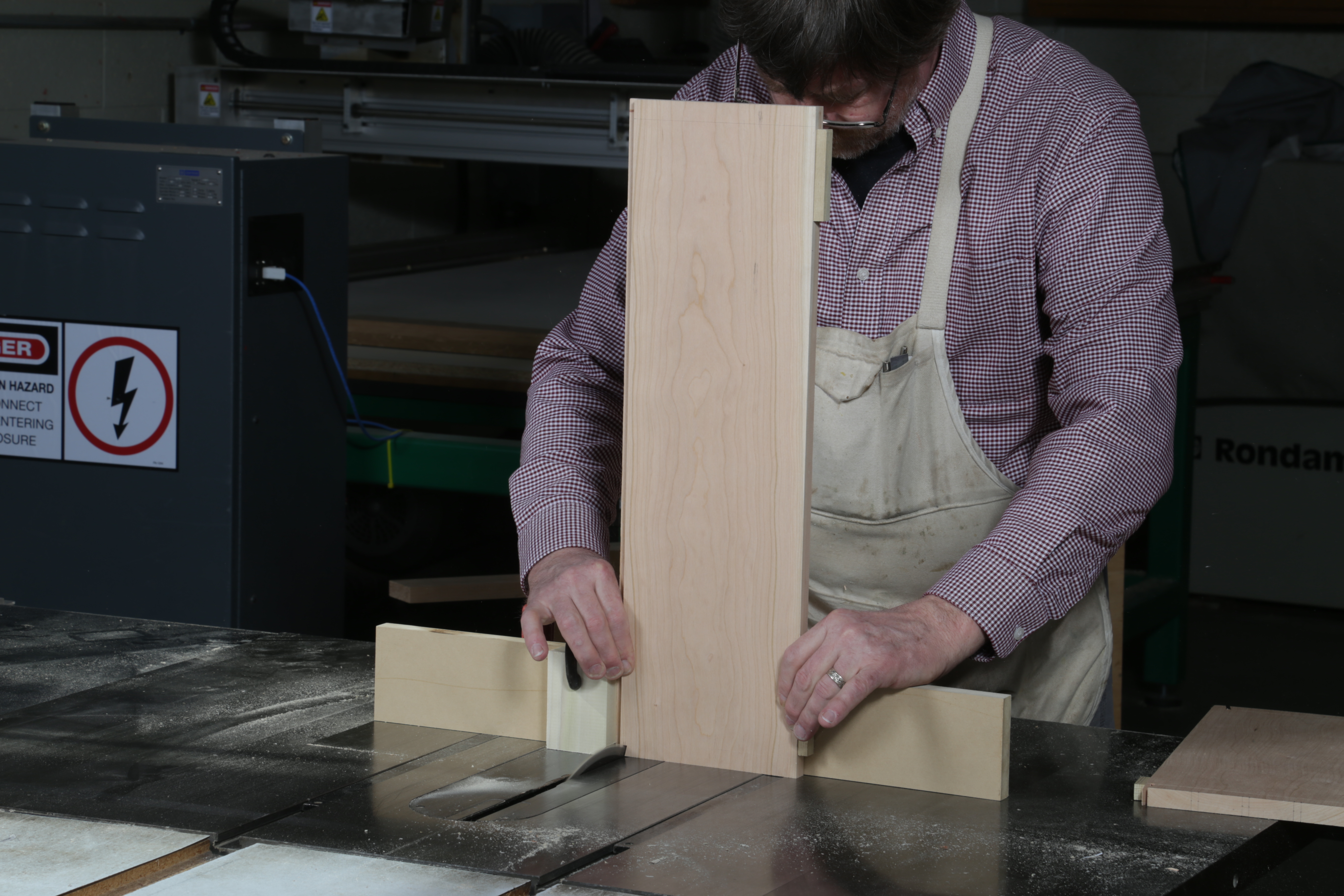 Push the workpiece against a stop and cut the first tail wall. Latta guides the piece using two miter gauges with a shared fence.