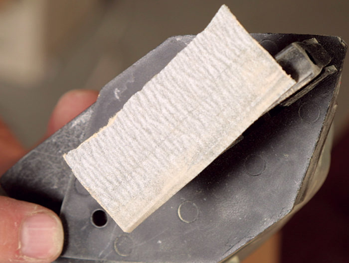 Adhesive backed sandpaper coming off the pad of a power detail sander
