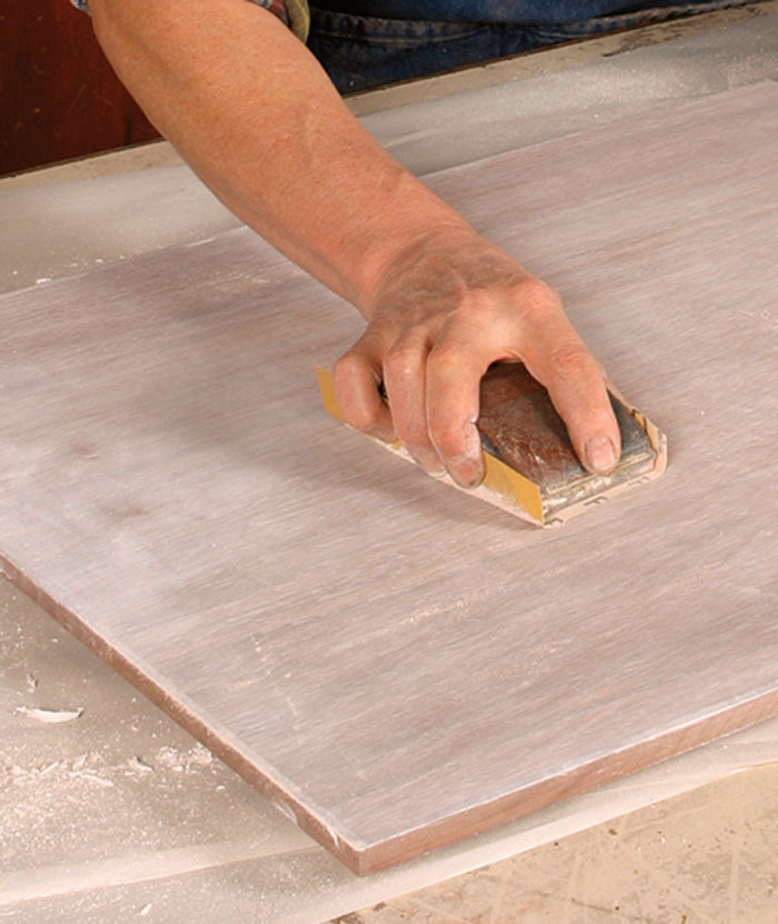 Sanding the board surface after packing the pores with plaster of paris.