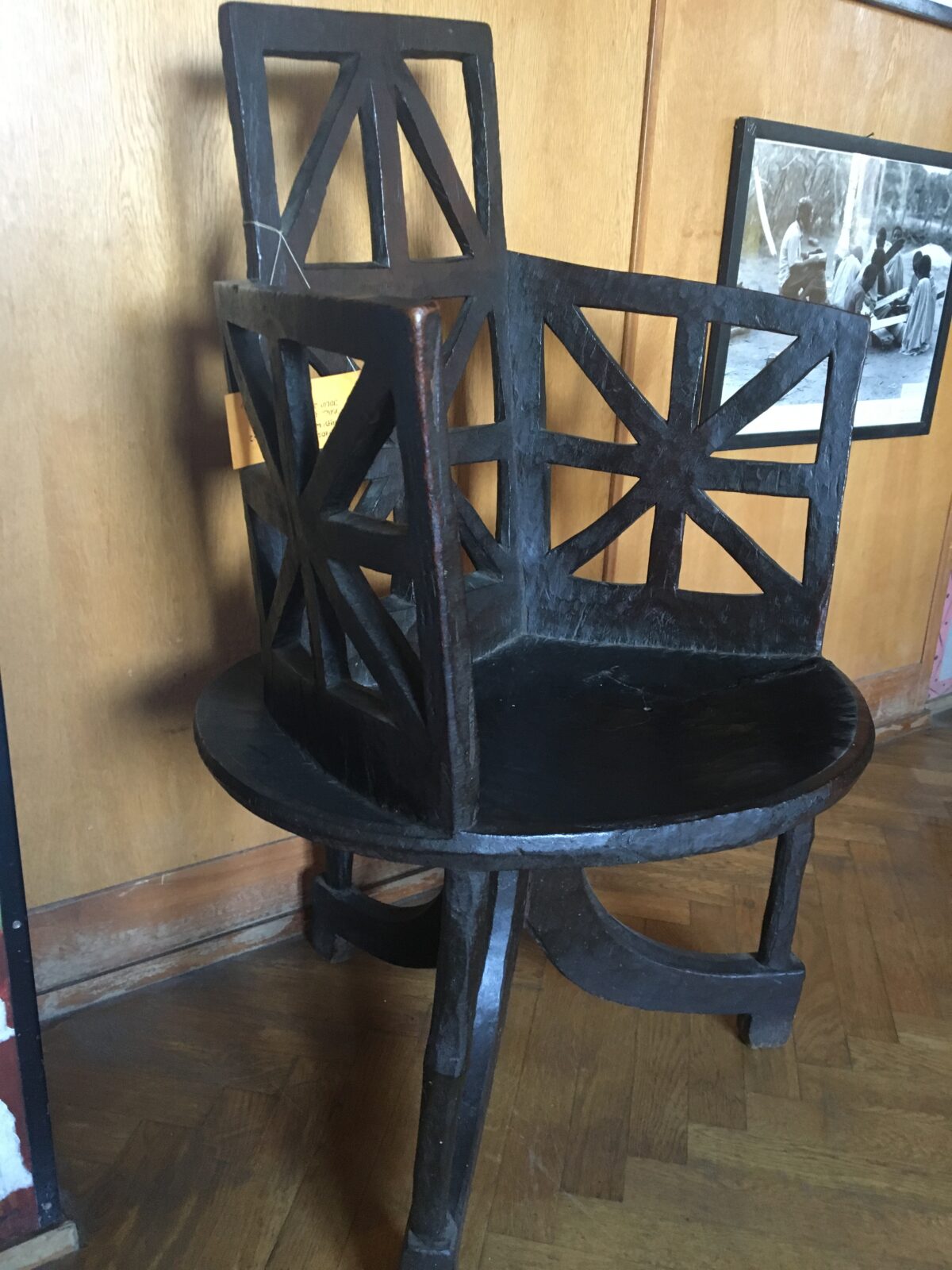 A very dark wooden chair with three swopping legs, a saucer-shaped seat, and a pierced-carving starburst pattern on its back rest and under its arms.