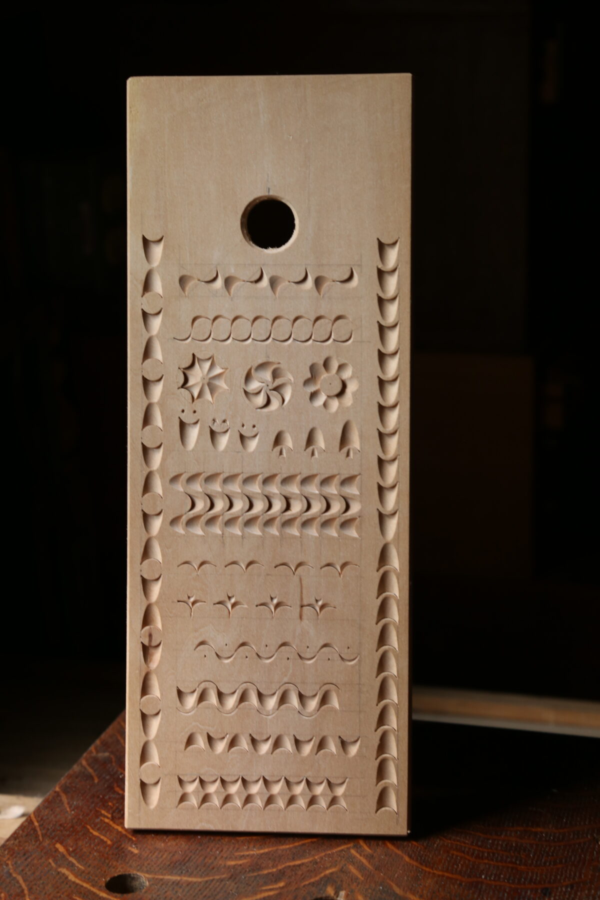A narrow basswood board featuring different patterns carved with a single gouge. Light rakes across it from the left, showing deep shadow contrasting against the light basswood.