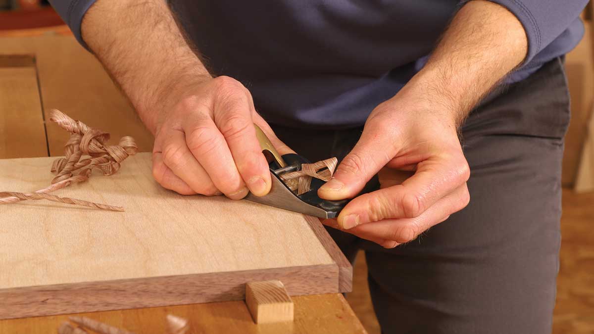 Flushing in two steps. Korsak uses two block planes to flush solid edging to a veneered panel. Here he takes a series of coarse shavings with the first block plane, stopping when the edging is about 1⁄64 in. proud of the panel.