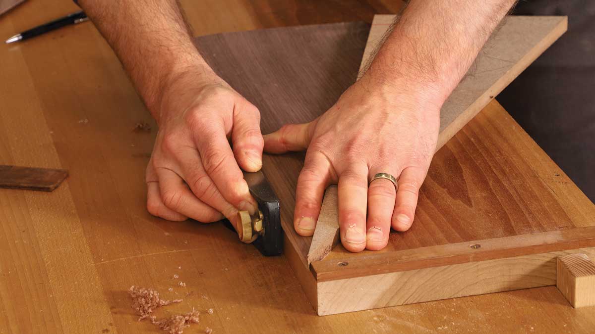 Support for a sunburst. To joint the vulnerable point of a wedge-shaped piece of veneer, Korsak uses his left hand both to hold the veneer flat and to add support behind it with an MDF backer.