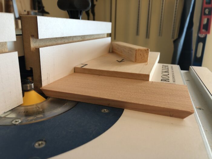 A piece of wood at the router table. Its ends are getting cut to 45 degrees.