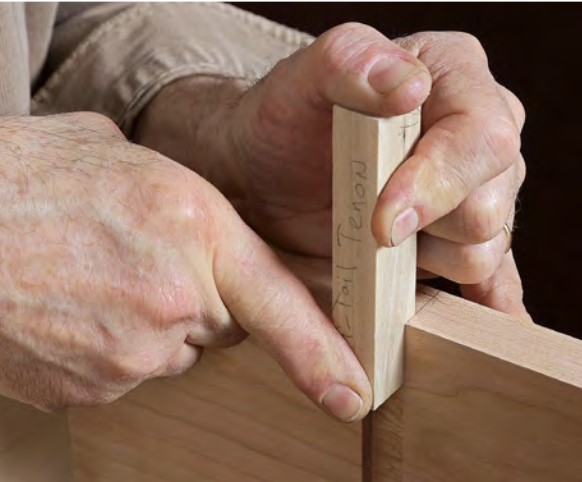 Two hands pressing a short block of wood into a recess in another board. The short block fits tightly in the recess.
