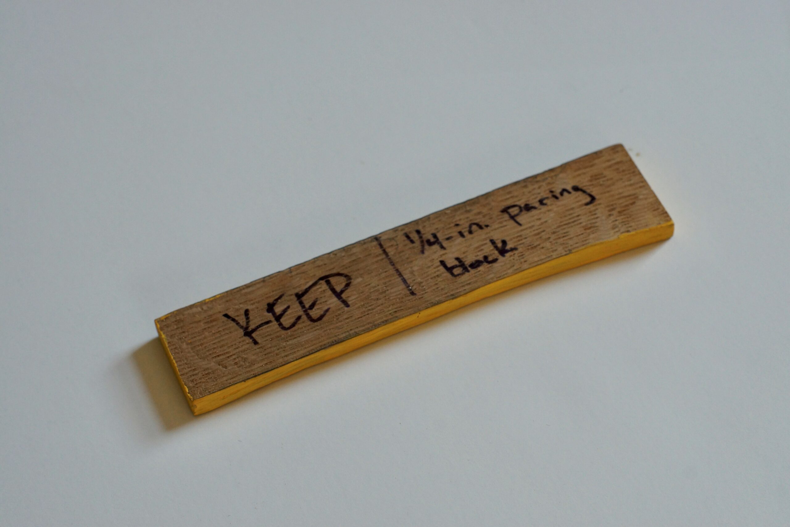 A thin, narrow, short, rectangular piece of wood with writing on it and yellow paint around its perimeter.