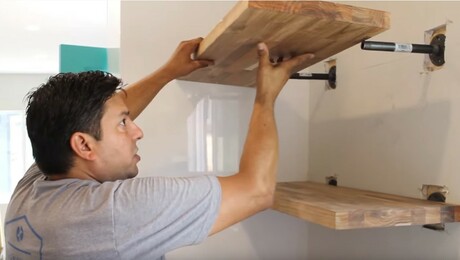 A man hangs DIY shelves