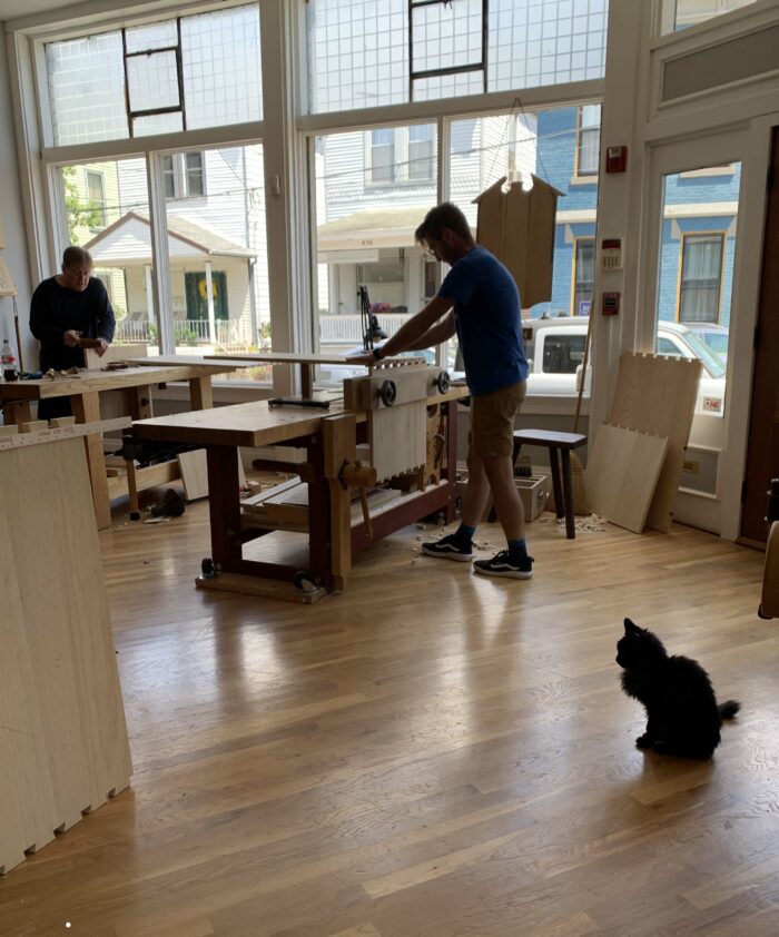 Woodworking students accompanied by a black shop cat.
