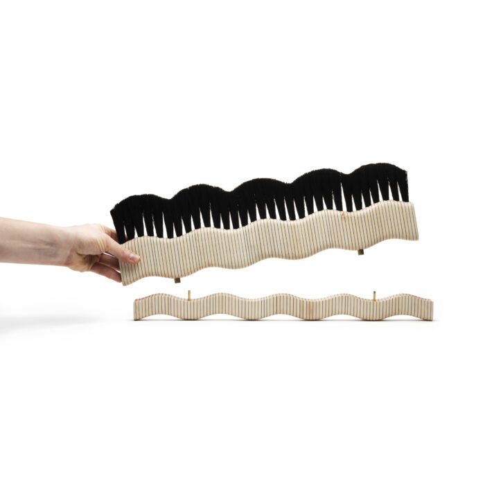A brush shaped like waves with a hand lifting it off of a base of matching shape.