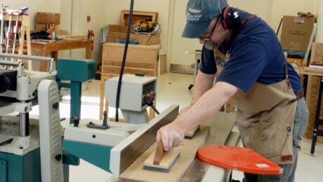 Mike Pekovich uses push pads to feed a piece of lumber through a jointer.
