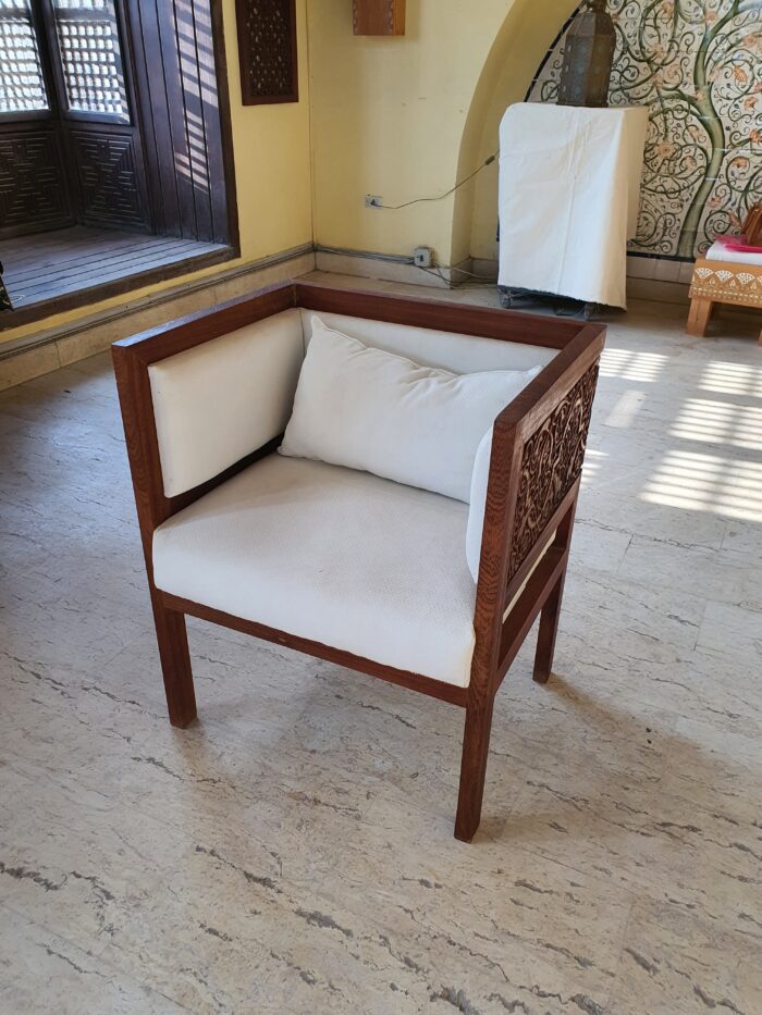 A hand-carved chair with a floral design and white upholstery by Mirna ElTatawy.