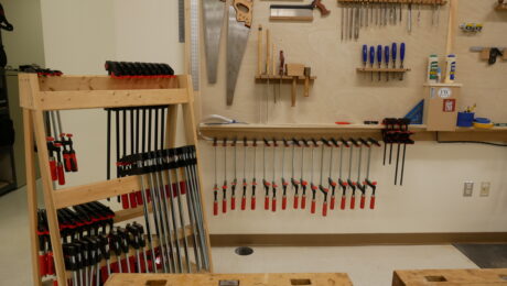 A clamp rack next to a hanging clamp shelf in the Fine Woodworking shop