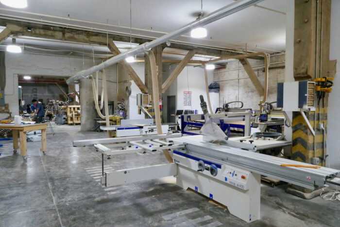 The Ottra Gallery wood shop, including a wide jointer and planer, a panel table saw, shapers, a long bar clamp dock, and a vast CNC machine.
