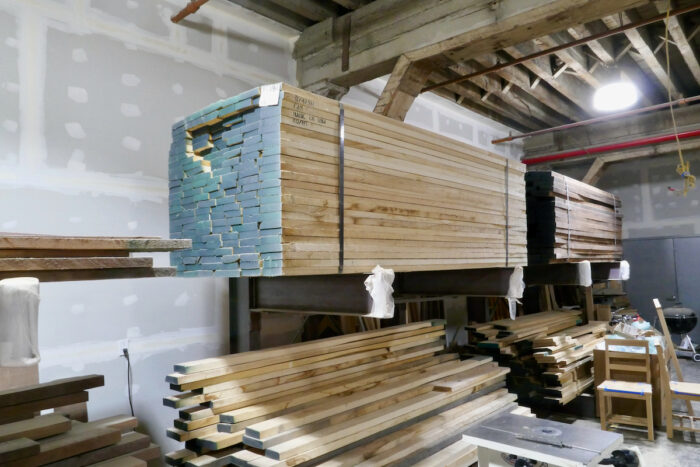 The Ottra Gallery wood shop, including a wide jointer and planer, a panel table saw, shapers, a long bar clamp dock, and a vast CNC machine. A stack of lumber sits elevated against the wall.