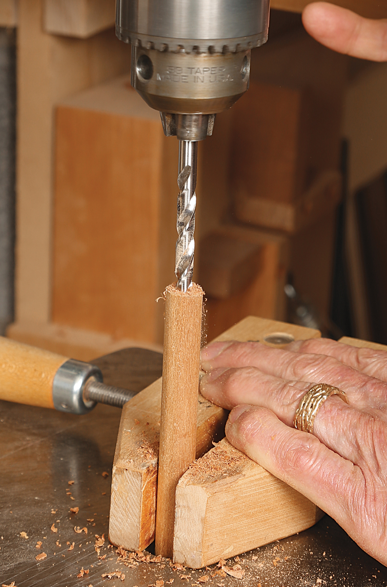 Clamp your dowel tightly in a hand screw, and drill a hole the same size or slightly larger than the diameter of the intended drill bit.