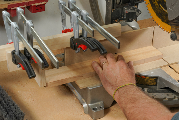 A piece of wood is being cut at a miter saw. There are stop blocks to assure consistent cutting. 