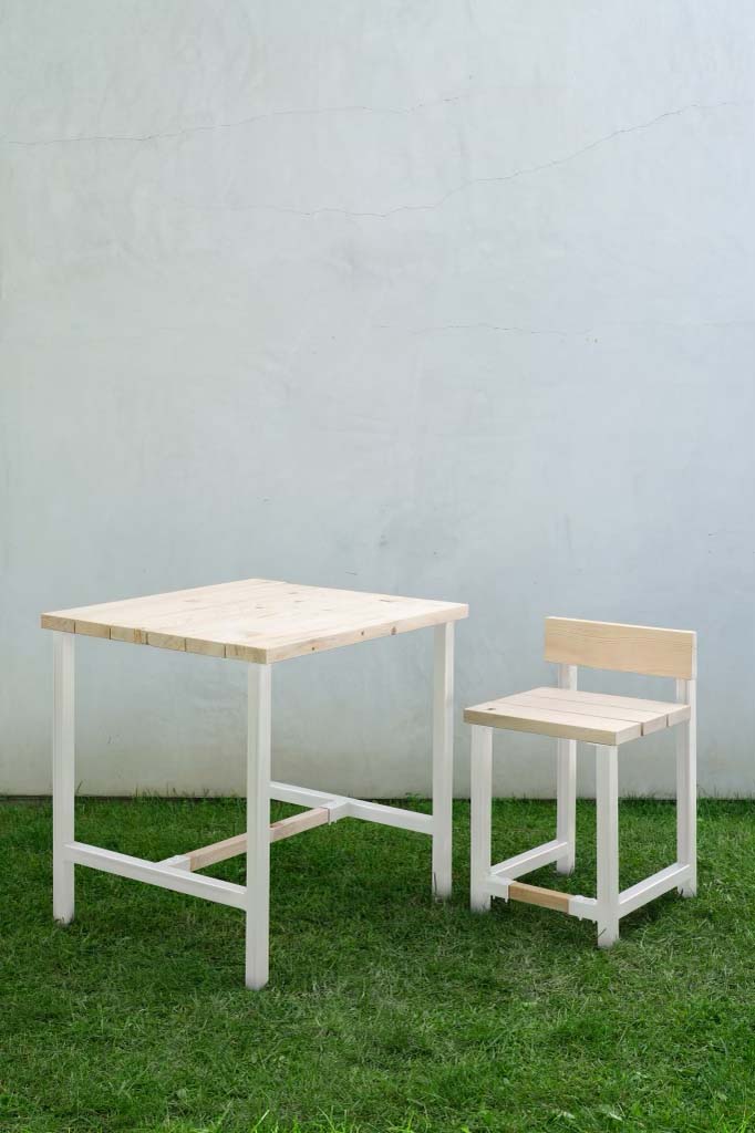 A table and chair made of wood with white legs sit on a green lawn. 