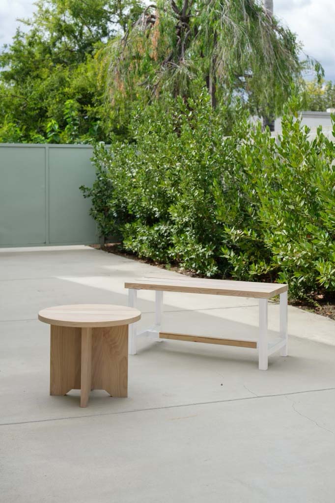 A verdant background overlooks a photo of two tables. One round and entirely wooden, while the other is rectangular with a white base.