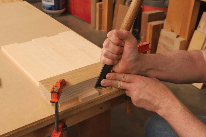 The author uses a chisel to slice more of the wood away.