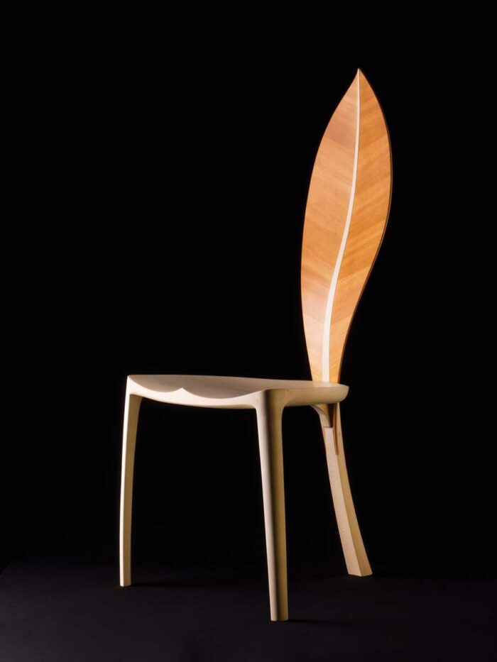 A three legged chair where the third leg is the stem of a leaf. The leaf creates the back rest of the chair.
