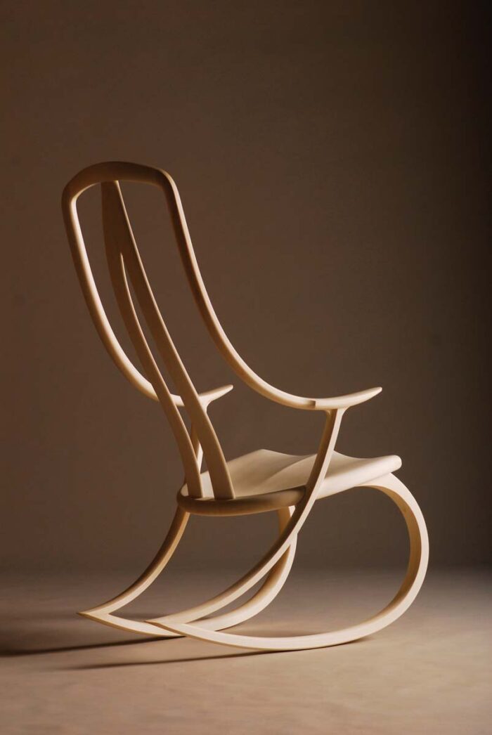 A photo of an s-shaped rocking chair. The way the photo is lit, it looks like the chair is looking into the distance longingly.