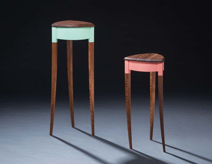 Two walnut end tables with three swaying legs. One tables apron is painted blue and the other table in pink. 