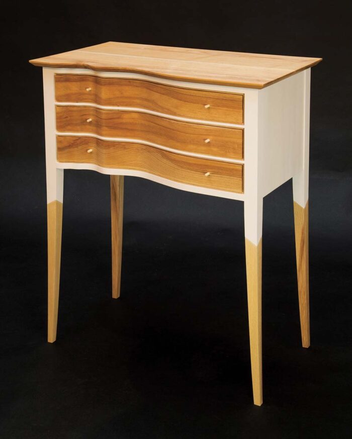 A sideboard with three wavy, sculpted drawers. Made of ash and painted with a cream color, with angled transitions on the paint termination.