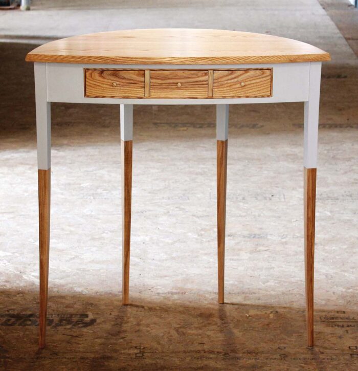 A side table with three ash drawers is painted with a soft, white color on the apron and top third section of each leg.
