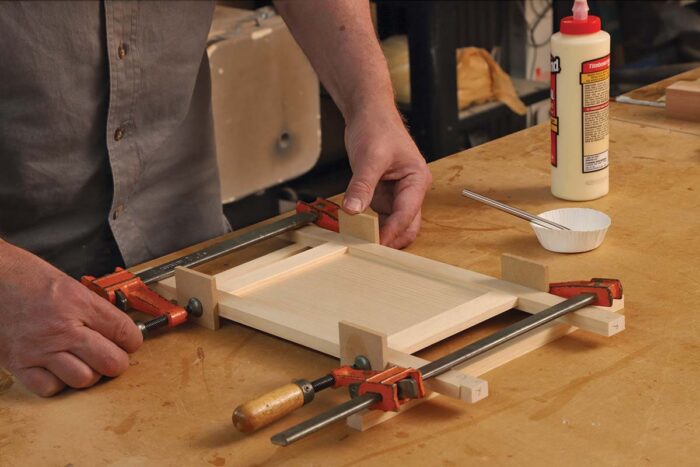 A door is being glued up. Two pieces horizontally and two pieces vertically create a parameter that a piece of wood sits it to create the frame and panel door.