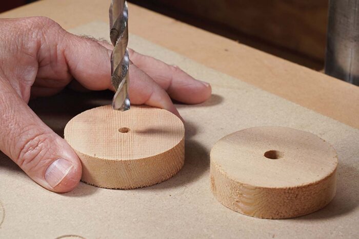 Asa uses a drill press to resize the holes left by the circle cutting jig.