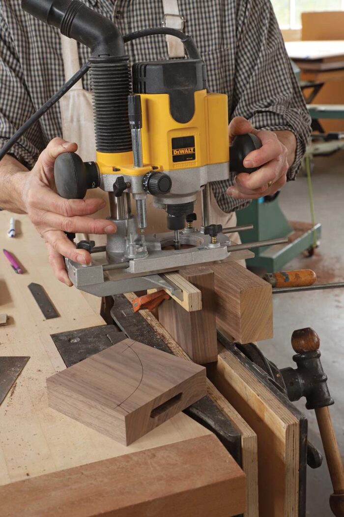 Tom uses a plunge router to make a mortise in a square block that will become the corbel of the table. 