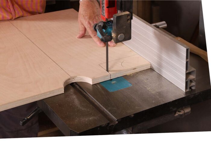 Beth uses a bandsaw to notch out the corner of a sheet of plywood.
