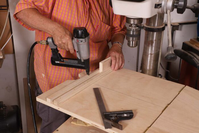 Beth uses a brad nailer to secure two strips of plywood that will sandwich a spacer block. 