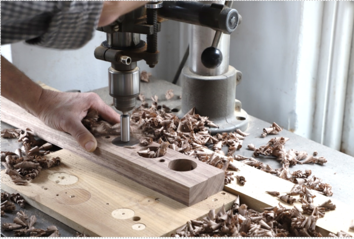 Tom drills several large holes in a walnut board with a drill press.