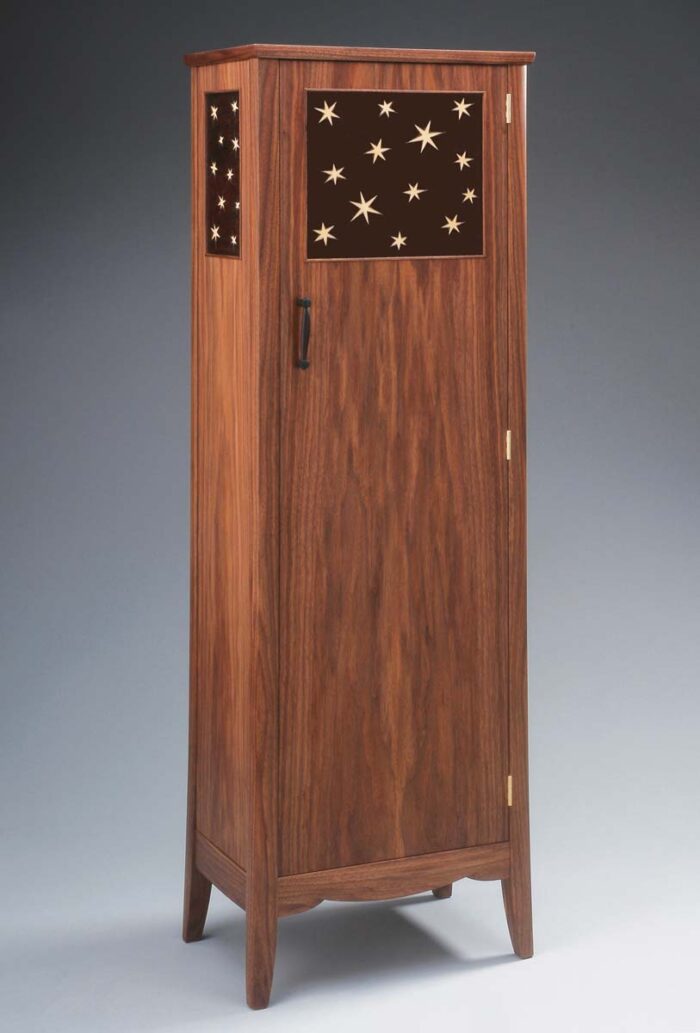 A tall cabinet with a slight taper and panels with star shaped marquetry. 