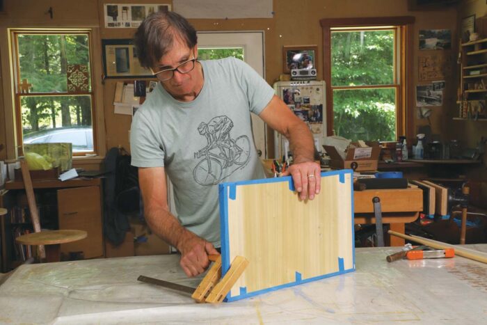 Tim uses an F style clamp to hold the glued up lumbercore panel upright, allowing for air flow on both sides. 