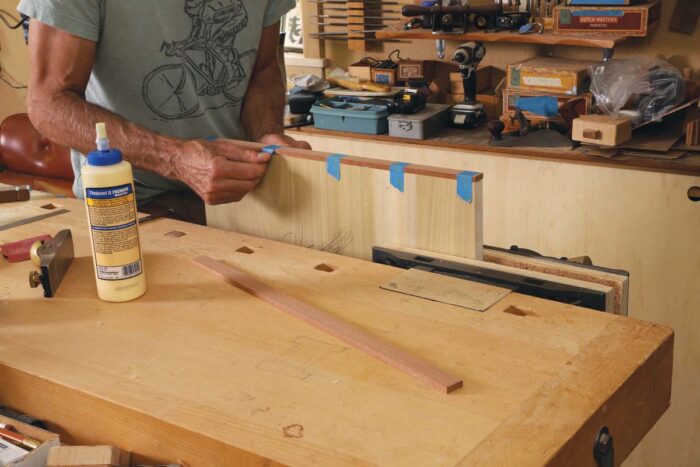 Tim uses blue scotch tape to secure 3/8 inch thick edge banding to the lumber core panel. 