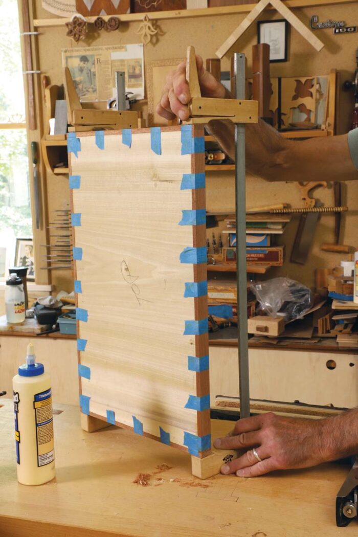 Tim clamps the edges of the edge banding to the panel, focusing on where end grain meets long grain. 