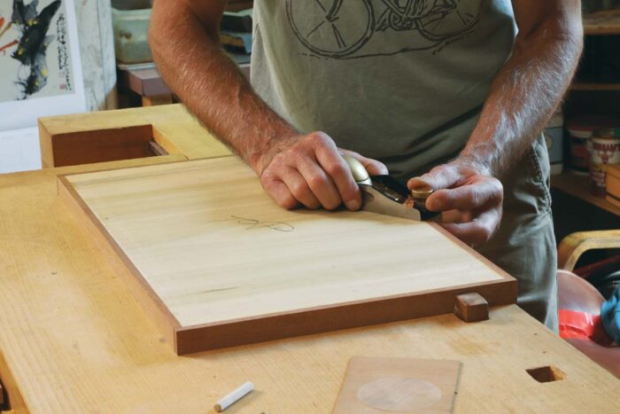 Tim uses a block plane to flush the overlap of edge banding flush to the rest of the panel. 