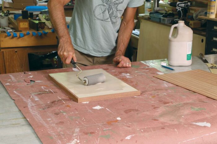 Tim uses a pain roller to apply unibond one glue to the surface of the panel, in preparation for the final veneer. 