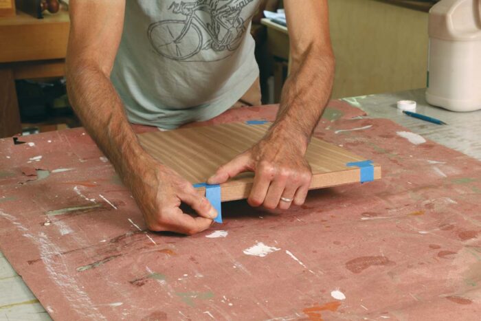 Tim secures the mahogany veneer over the panel with blue tape.