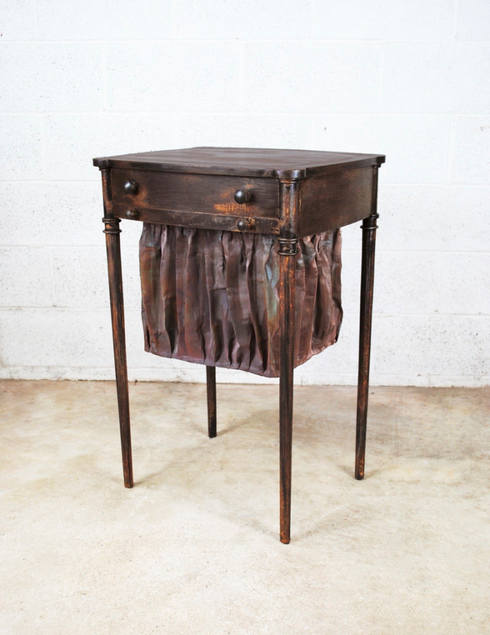 A metal sewing table with copper mesh hanging below, draped to make it look like fabric. 