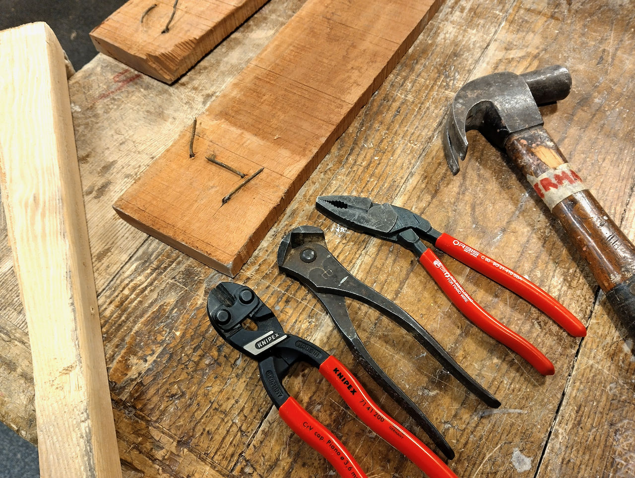 A hammer nippers, and pliers lying in front of a reclaimed board.