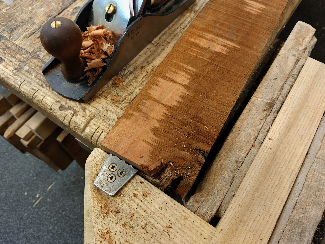 A partially planed reclaimed board with a jack plane sitting next to it. Surfacing reveals a reddish brown color. 